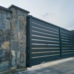 Wide black automatic sliding gate with remote control installed by Expert Garage Doors.