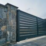 Wide black automatic sliding gate with remote control installed by Expert Garage Doors.